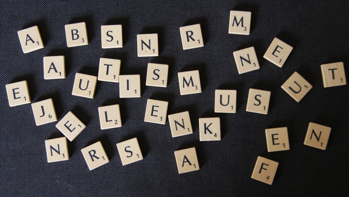 Zahlreiche Scrabble Spielsteine die scheinbar wahllos durcheinander liegen und in den sich das Wort Autismus verbirgt.