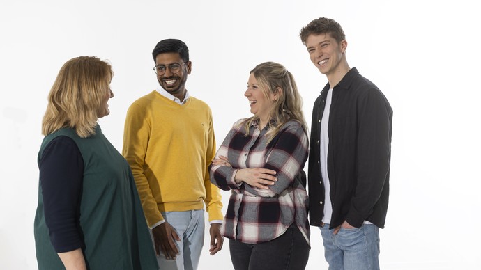 Vier Menschen stehen nebeneinander in Alltagskleidung und schauen sich lachend an. Vier Menschen stehen nebeneinander in Alltagskleidung und schauen sich lachend an.