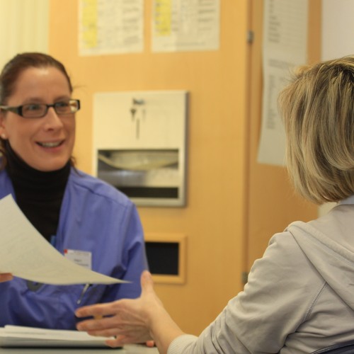 Die Krankenschwester reicht einer Patientin ein  Aufnahmeformular.