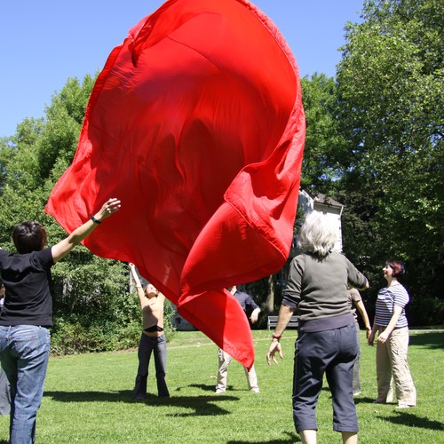 Eine Gruppe von Männern und Frauen wirft ein großes rotes Tuch in die Luft und versucht es wieder aufzufangen