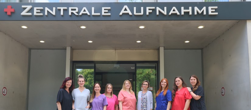 Das Aufnahmeteam steht vor der Rezeption der Zentrale Aufnahme. Über Ihnen der Hinweis "Aufnahme"