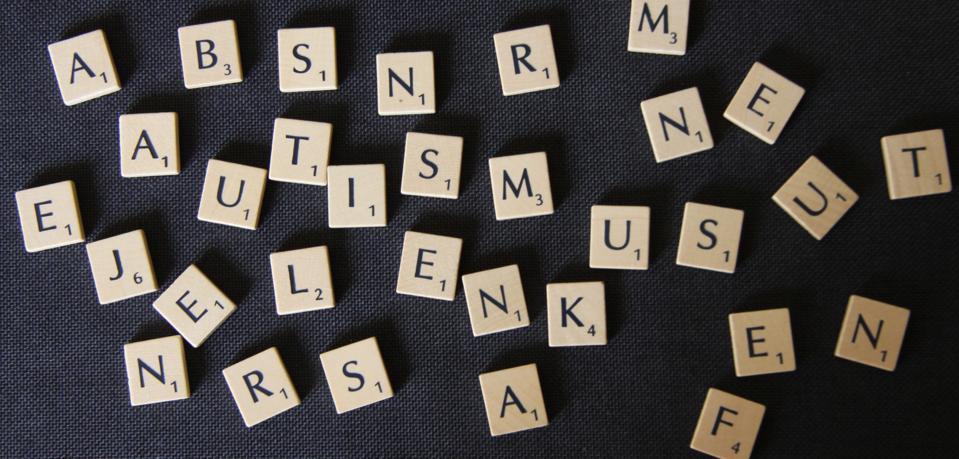 Scrabble Steine bunt durcheinander gewürfelt. Autismus ist bei genauem Hinsehen zu lesen.