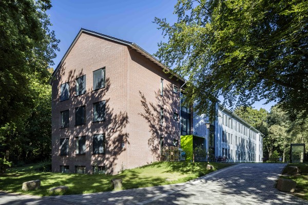 Ein langgezogener Gebäude mit Klinkerfassade davor und rechts davon Bäume