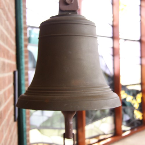 Eine Glocke, im Hintergrund angedeutet ein Kirchenfenster