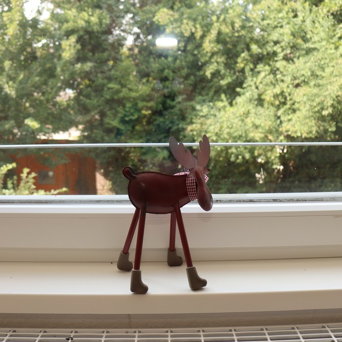 Ein Hirsch aus Metall steht auf einem Fensterbrett, dahinter ein begrünter Garten. (öffnet vergrößerte Bildansicht)