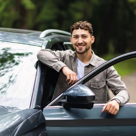 Mann lehnt an geöffneter Autotür und lächelt in die Kamera