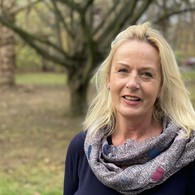 Eine blonde Frau mit buntem Schal schaut Lächeln in die Kamera. Eine blonde Frau mit buntem Schal schaut Lächeln in die Kamera.